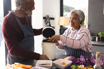 Senior biracial couple wearing aprons composting food waste in kitchen at home