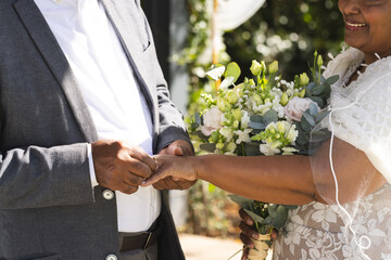 Midsection of senior biracial groom putting wedding ring on finger of bride - Powered by Adobe
