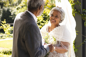 Happy senior biracial bride and groom during wedding ceremony in sunny garden
