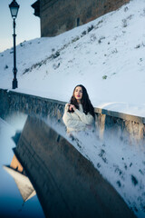 A girl in a white sweater poses looking towards the snowy landscape