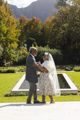 Fototapeta premium Happy senior biracial bride and groom dancing in garden at sunny wedding ceremony, copy space