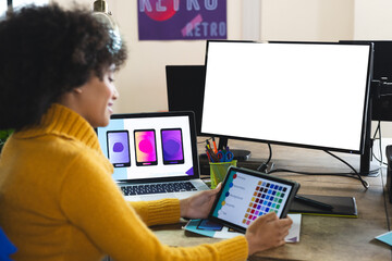 Happy african american female designer using tablet and computer with copy space at desk in office