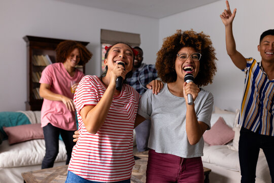 Happy diverse friends dancing and karaoke singing with microphone at home