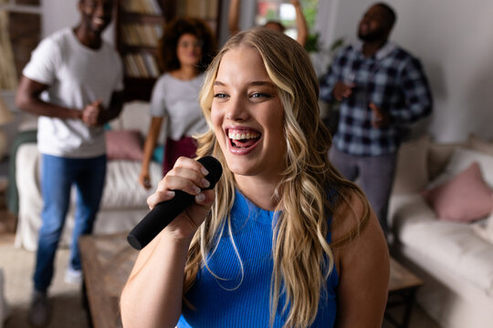 Happy diverse friends dancing and karaoke singing with microphone at home