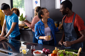 Happy diverse group of friends cooking and talking with drinks in kitchen