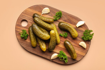 Wooden board with pickled cucumbers, parsley and garlic on orange background