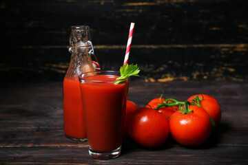 Glass and bottle of tasty tomato juice on black wooden background