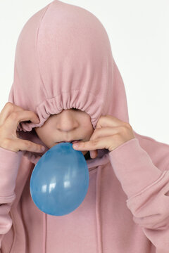 Portrait of preteen boy hiding his eyes under hood and inflating blue balloon