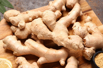 Wooden board with fresh ginger roots and bowl of dried powder on dark background, closeup
