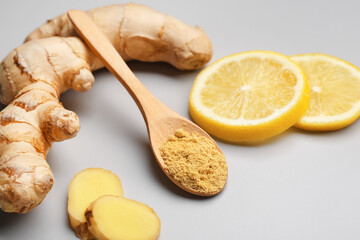 Fresh ginger root, slices of lemon and wooden spoon with dried powder on grey background