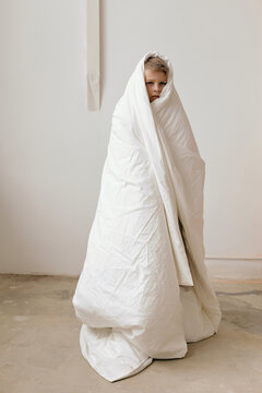 Picture of boy standing wrapped in white duvet against white wall background