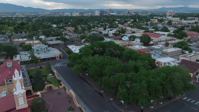 Old town Albuquerque square. Aerial shot of trees in center park with adobe buildings. Albuquerque, New Mexico skyline in distance at dawn.