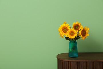 Vase with beautiful sunflowers on table near green wall in room