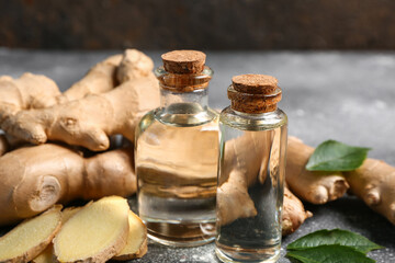 Bottles of ginger cosmetic oil and leaves on grey table