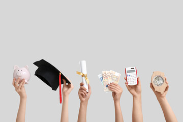 Female hands holding piggy banks, graduation cap, diploma and money on grey background. Student...