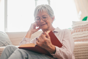 Portrait of relaxed retired senior woman sitting on the floor at home while reading a book enjoying...