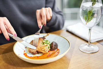 Lunch in a restaurant, a woman cuts delicious duck leg su-vide, with bulgur and onion marmalade. Barbecue restaurant menu, a series of photos of different meats