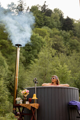Young woman bathing in hot tub heated by firewood, resting in the mountains. Concept of recreation...