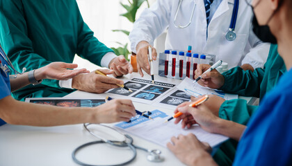 Medical team having a meeting with doctors in white lab coats and surgical scrubs seated at a table discussing a patients working online using computers in the medical industry