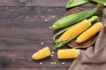 Board with fresh corn cobs on dark wooden table