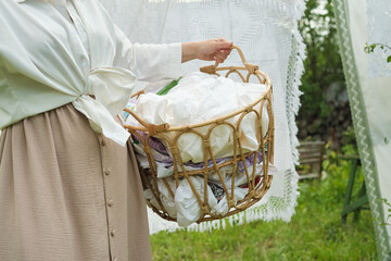photograph showing an unrecognizable woman with a full laundry basket, standing outdoors with...