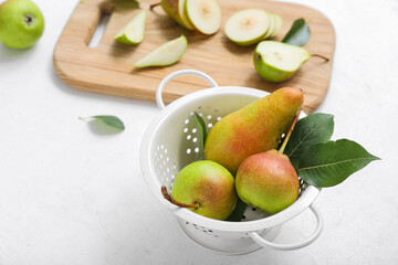 Colander with ripe pears on white table