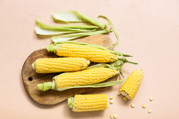 Wooden board with fresh corn cobs on beige table