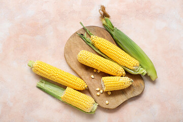 Wooden board with fresh corn cobs on beige table