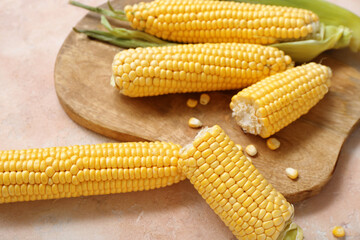 Wooden board with fresh corn cobs on beige table, closeup