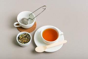 Cup of hot tasty green tea, strainer for tea in empty white mug and herbal tea leaves in ceramic...