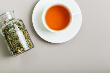 Glass jar filled with aromatic tea leaves and white ceramic cup of hot tasty tea from above on light background.