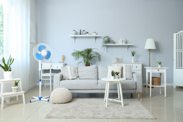Interior of light living room with grey sofa and floor fan