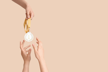 Female hands receiving medal on beige background