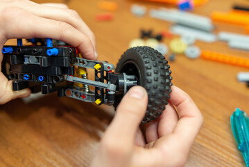 Close up of boy attaching wheel to his model made of engineering constructor. Playing with toys for...