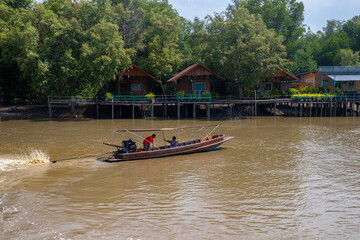 A motorboat sailing down a river in the late afternoon with village on  the mangrove in the...