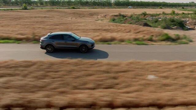 Aerial side shot of a grey luxury SUV Sport car accelerating  on a country tarmac road surrounded by golden wheat fields
