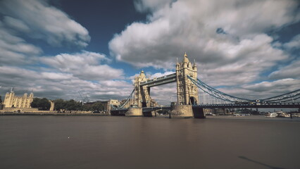 Tower Bridge over river Thames with sailing boats ships and London Tower Fortress lit by sunlight under blue sky. Soft clouds fast motion in blue sky. Travel recreation concept.
