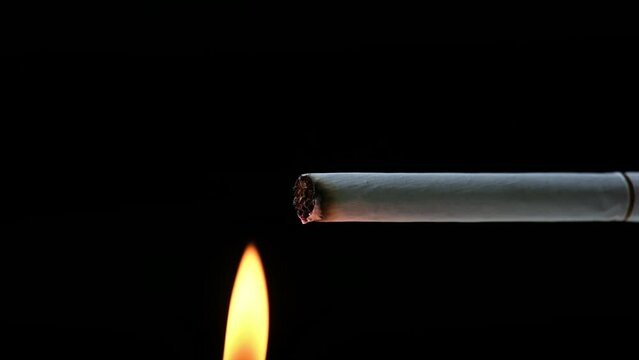 Lighter fire lit up cigarette in Black background. Smoking kills concept. Cigarette tip burnt into ashes by flame and then emit smoke