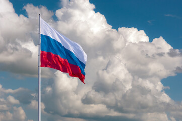 Waving the Russian flag against a blue sky with expressive white clouds on a summer day. State flag of the Russian Federation