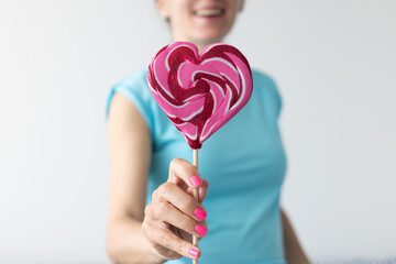 Smiling woman with pink nails propose the big pink lollipop. Closeup.