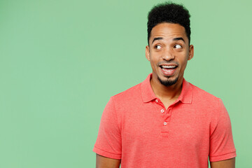 Young happy surprised shocked amazed man of African American ethnicity he wearing pink t-shirt look aside on workspace area mock up isolated on plain pastel light green background. Lifestyle concept.