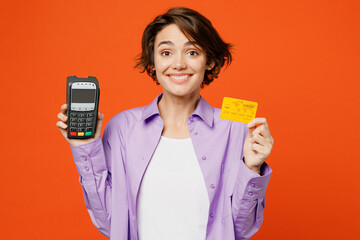 Young caucasian woman she wear purple shirt white t-shirt casual clothes hold wireless modern bank payment terminal to process acquire credit card isolated on plain orange background studio portrait.