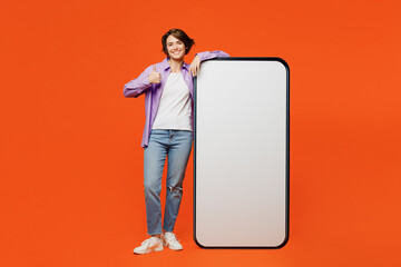 Full body smiling young woman she wear purple shirt white t-shirt casual clothes big huge blank screen mobile cell phone smartphone with area show thumb up isolated on plain orange background studio.