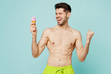 Young happy sexy man wear green shorts swimsuit relax near hotel pool hold in hand eat icecream do...