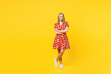 Full body young smiling cheerful happy caucasian woman she wear red dress casual clothes hold hands crossed folded look camera isolated on plain yellow background studio portrait. Lifestyle concept.