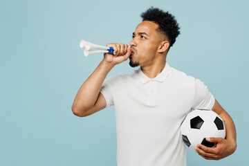 Side view young man fan wear basic t-shirt cheer up support football sport team hold in hand soccer ball blowing pipe look camera watch tv live stream isolated on plain pastel blue color background.
