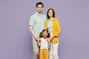 Full body smiling cheerful young parents mom dad with child kid daughter girl 6 years old wear blue yellow casual clothes looking camera posing isolated on plain purple background. Family day concept.