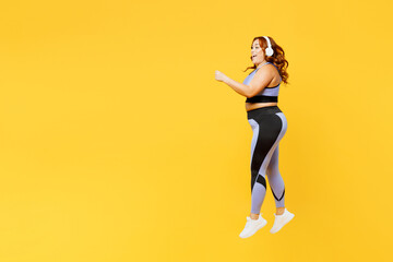 Fototapeta na wymiar Full body young plus size fat fit woman wear blue top warm up train listen music in headphones jump high do aerobic exercise isolated on plain yellow background studio home gym. Workout sport concept.