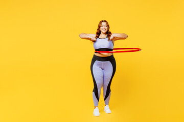 Full body young fun chubby plus size big fat fit woman wear blue top warm up training using hula hoop for waist weight loss isolated on plain yellow background studio home gym. Workout sport concept. - obrazy, fototapety, plakaty