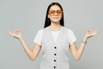 Young latin woman wear white t-shirt gray vest glasses hold spreading hands in yoga om aum gesture...